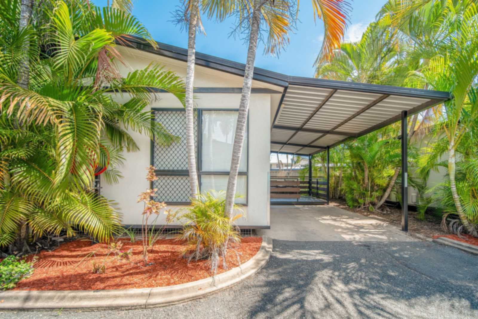 Apartment with an undercover carport among palm trees at Emerald Motel Apartments